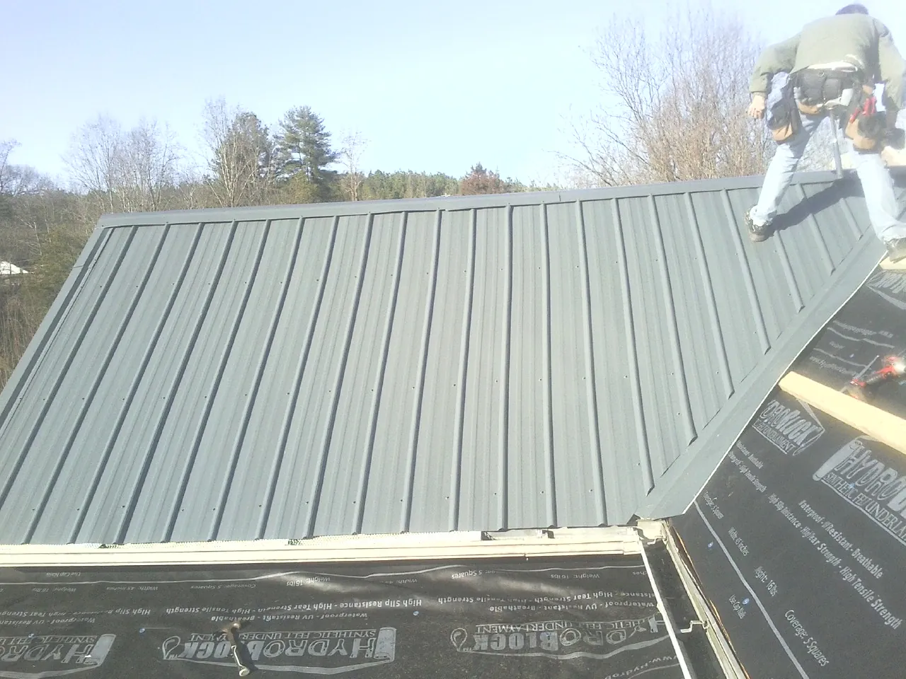 Crew installing dark green standing seam panels over synthetic underlayment in Weston